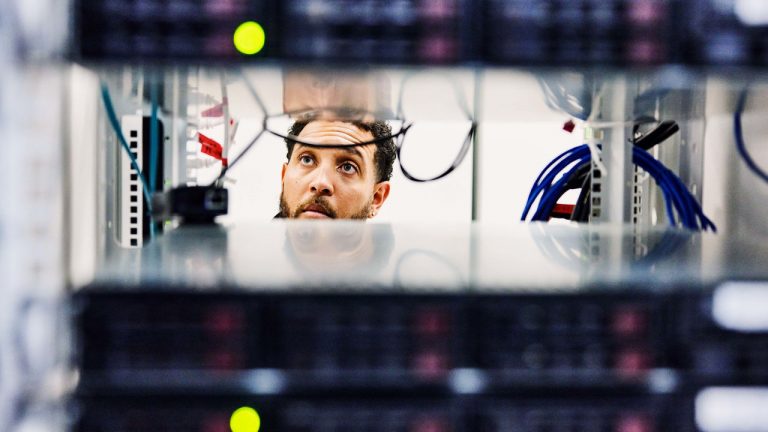 An IT professional is examining a server rack through its gaps.